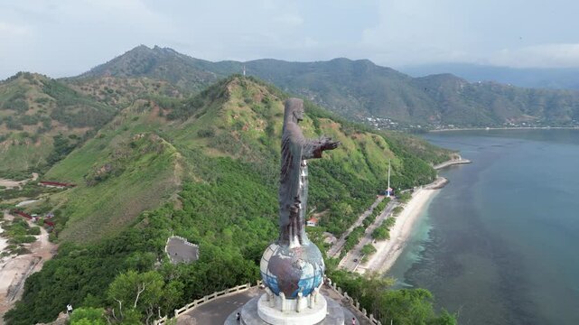 A towering christ statue with lush hills and coastline in timor-leste, aerial view
