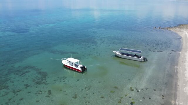 Boats anchored in shallow clear water along a quiet beach in Dili, Timor-Leste during the day