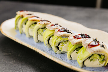 Eel sushi roll with creamy filling, topped with savory sauce and sesame seeds on a stylish plate