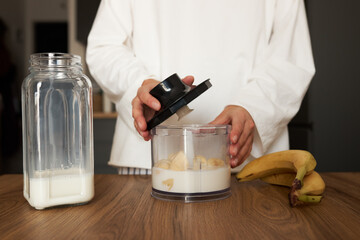 Woman preparing milkshake with blender at the kitchen