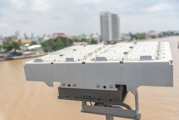 Mini photovoltaic or solar cell panel and floodlight led installed on metal pole against sunset