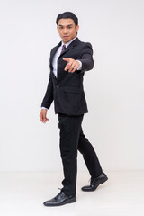 Full-body Portrait of a handsome asian businessman in a suit and tie, pointing at camera with his...