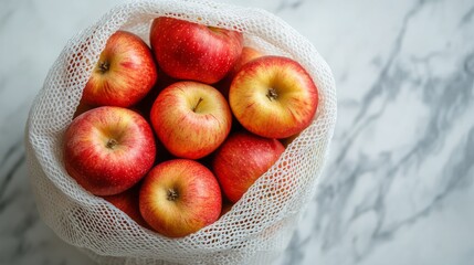 Apples in a white mesh bag lie on a marbled surface.