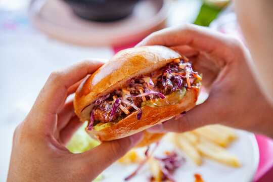 Hands holding fried chicken burger in brioche potato bun with coleslaw.