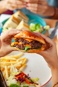 Girl holding a double patty smashed beef burger in a cafe restaurant eating with friend.