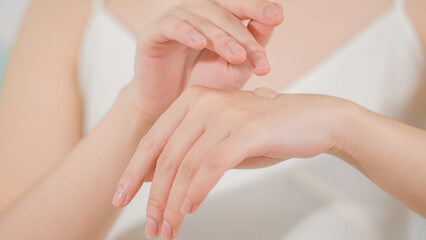 Fototapeta premium Frontal close-up photo of a woman wearing a white strapless dress preparing to apply a drop of lotion to the back of her hand. Advertising template, blank space for adding design elements