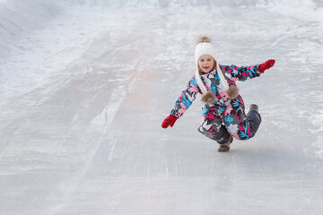 A little girl rides on an ice slide in winter.