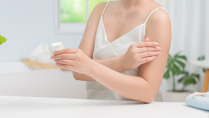 Fototapeta premium The promotional template photo for body care product with bathroom concept, was taken from front view on minimal background. Young woman applying lotion to her arms. Front view, vacant space
