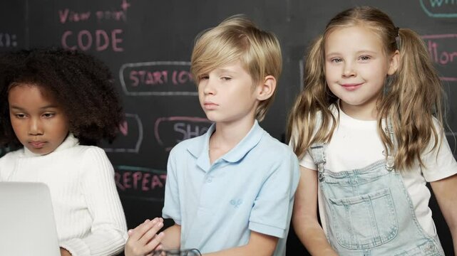 Smart girl using laptop programing engineering code with diverse friends ay table with microchip and main board scatter around in STEM classroom at blackboard written with coding prompt. Erudition.