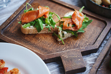 Sandwich with red fish and green salad on a wooden tray.