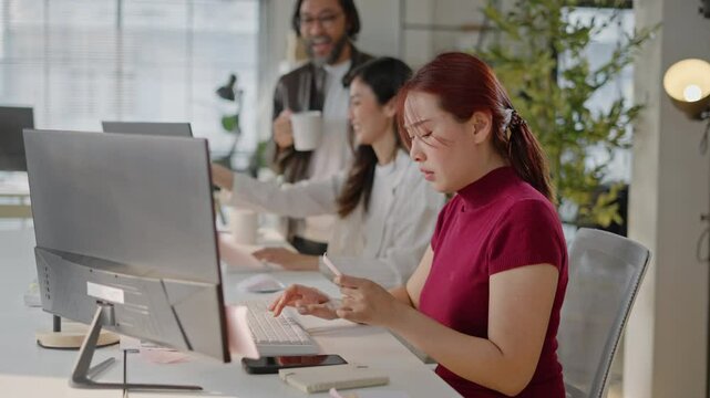 Stressed Asian businesswoman with headache and noisy people in office.