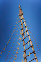 Gazing up at a tall wooden mast adorned with ropes set against a vivid blue sky