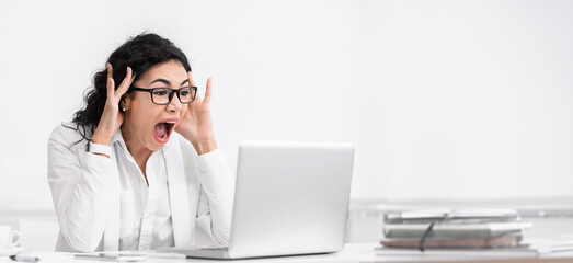 Shocking News. Amazed mexican businesswoman looking at laptop computer with open mouth and eyes. Copy space