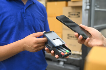 Cropped shot of customer making contactless payment with smartphone and receiving parcel box from delivery man