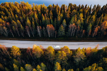 Aerial view Caravan trailer or Camper rv on the road by fall tree woods and blue lake water in Finland.
