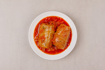 Two cabbage rolls stuffed with minced meat in vegetable gravy on a white platter on a gray background top view