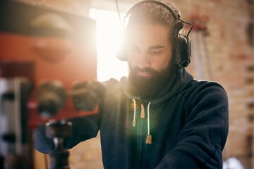 Woodworker using a drill press in his studio. He wears hearing protection and looks down focused on the machine that is drilling into some wood