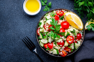 Vegetarian Tabbouleh Middle Eastern salad with bulgur, tomatoes, cucumbers and parsley.. Black background, top view