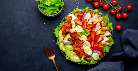 Cobb salad with chicken, tomatoes, eggs, bacon, avocado and lettuce, black background, top view
