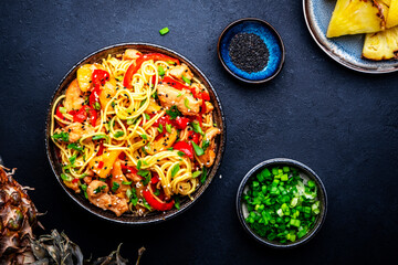 Stir fryed noodles with chicken slices, pineapple, red paprika, onion, soy sauce, garlic, ginger and sesame seedsl. Black background, top view