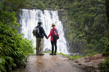 Couple holding hands and looking at beautiful Marokopa Falls. Waikato. New Zealand.