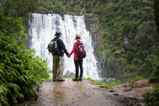 Couple holding hands and looking at beautiful Marokopa Falls. Waikato. New Zealand.