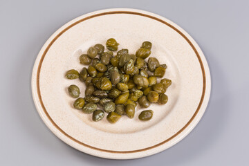 Pickled capers on a saucer on a gray background