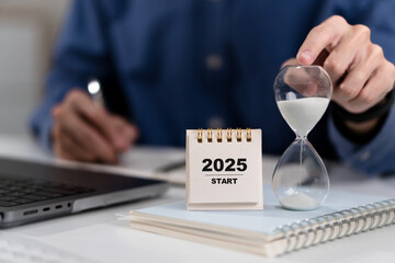 Hand points to hourglass and 2025 calendar to start counting 2025. Happy New year background. Setup objective target business cost and budget planning of new year concept.