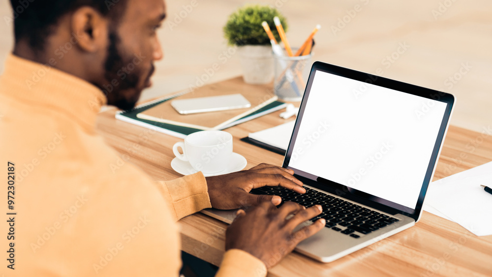 Poster Mock Up Template. Rear view of black man working on laptop with blank screen, typing on keyboard, copyspace