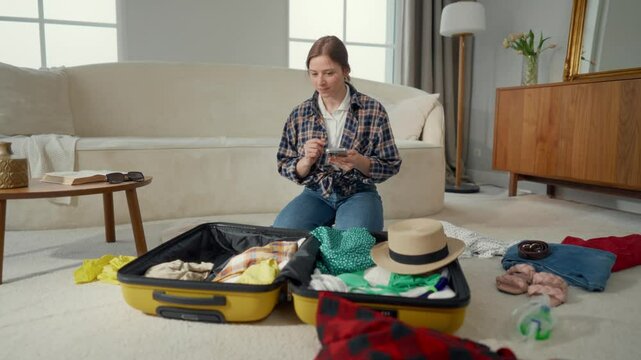 Woman preparing to trip, looking for information in internet, packing suitcase. Girl with smartphone preparing clothes and things for summer vacation on sea coast, holidays and tourism, lady at home