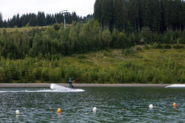 A person water skiing on a lake surrounded by forests on a cloudy afternoon