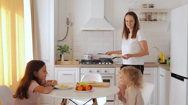 Delighted mom serving healthy omelets to her kids at the kitchen table while the family enjoys nutritious breakfast together indoors on peaceful morning