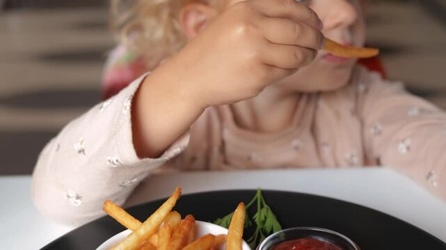 Delicious grilled meat. Unhealthy junk food. Little toddler blonde wavy haired girl eating grilled potatoes dish with cutlet and sauce enjoying junk food at restaurant