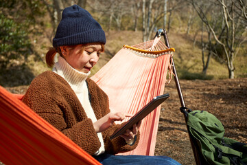 ハンモックに座ってタブレット端末を操作する女性