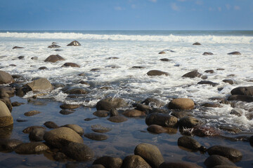 Serene coastline of El Tunco, El Salvador with waves gently lapping over smooth stones at afternoon light