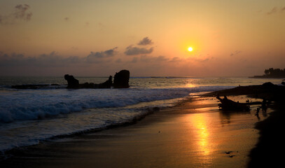 Sunset at El Tunco beach in El Salvador with waves crashing and silhouettes of rocks under vibrant sky