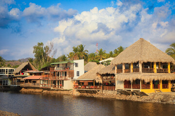 Fototapeta premium Experience the vibrant atmosphere of El Tunco, El Salvador, with colorful buildings lining the tranquil waters under a bright sky