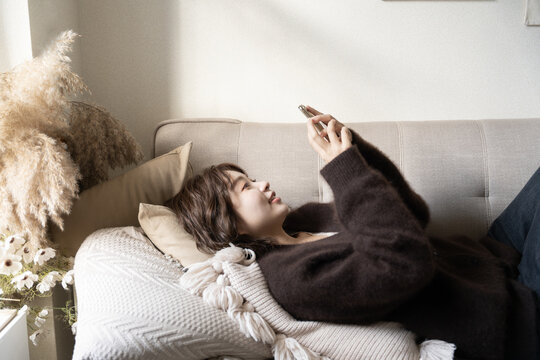 ソファでスマホを見ながら笑っている女性