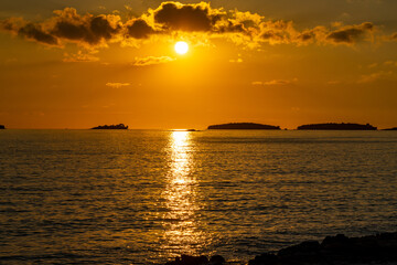 Dramatic dark clouds over sunset in the sea. Orange-red sky and reflections of the sun in the glistening water