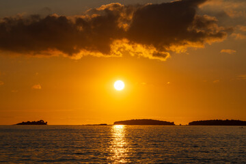 Dramatic dark clouds over sunset in the sea. Orange-red sky and reflections of the sun in the glistening water