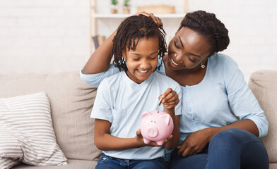 African Mother And Daughter Putting Coins Into Piggy Bank At Home. Free space