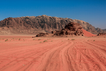 Vast red sands and dramatic rock formations in the Wadi Rum Desert at mid-day under a clear blue sky