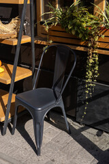 A black metal chair beside wooden shelves and plants in a sunlit outdoor setting