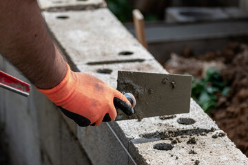 A bricklayer works on blocks to build a wall on a construction site with concrete, a trowel, a...