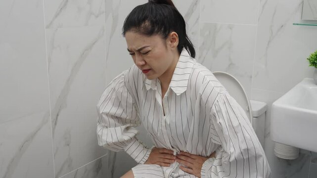 woman sitting on toilet bowl and holding her painful Stomach in the bathroom