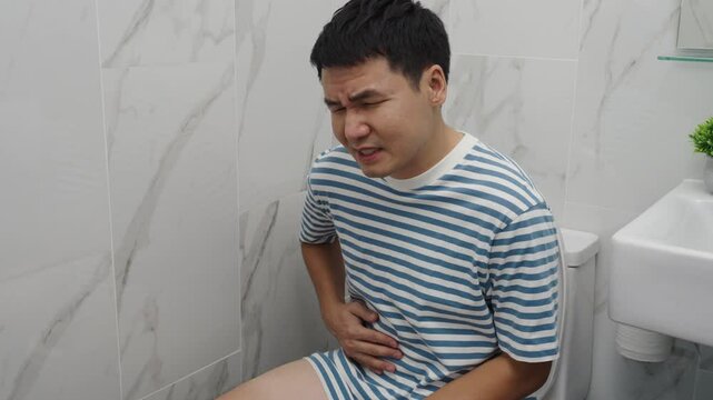 unhappy man with stomach issues sitting in toilet bowl in the bathroom