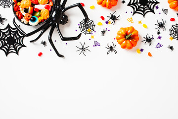 Frame of Halloween decoration spider full of candies, pumpkins, spiders web on white background.