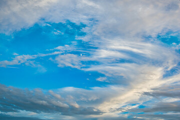 Blue sky with circling clouds and a small crescent moon in the middle.