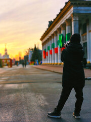 A teenage boy in a hat and jacket takes pictures of interesting historical places on a camera. Rear view in perspective