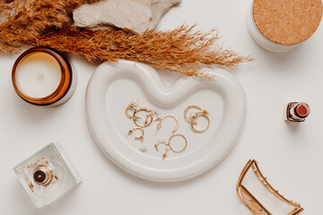 Feminine golden jewelry on ceramic tray or display with accessories, candle and cosmetics....